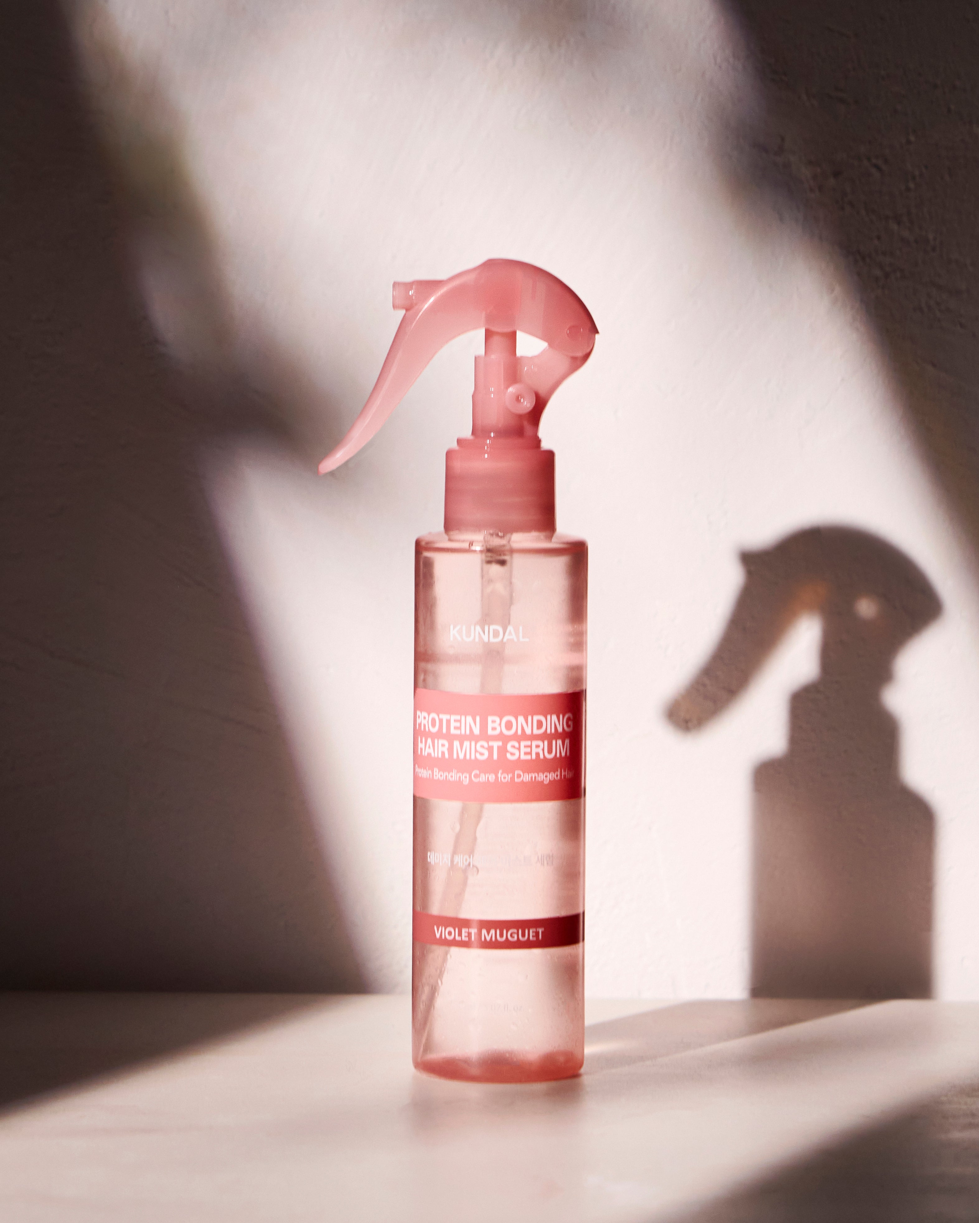KUNDAL Protein Bonding Hair Mist Violet Muguet in einer rosafarbenen Sprühflasche mit stilvollem Schattenwurf