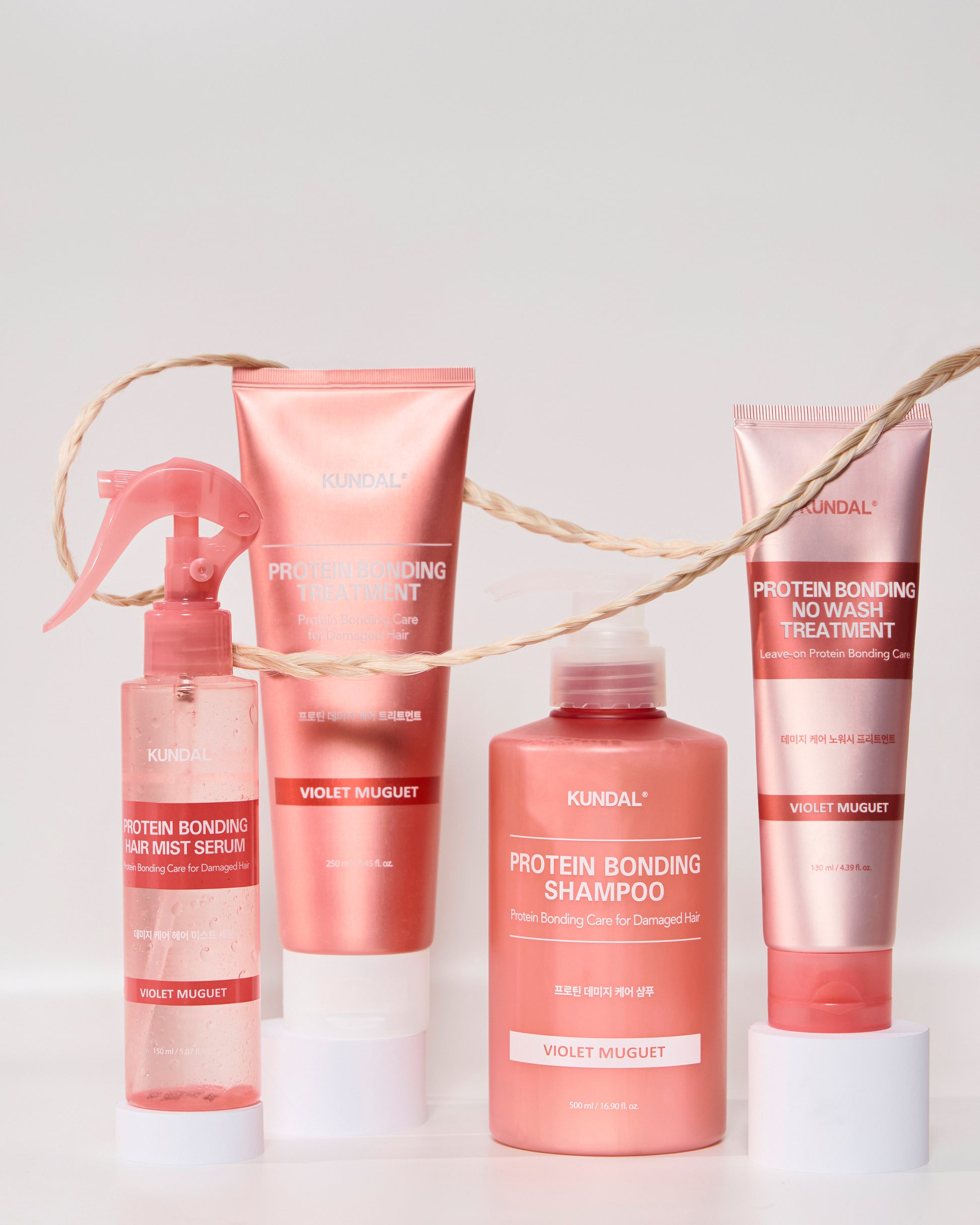 KUNDAL Protein Bonding Hair Mist Violet Muguet Sprühflasche neben Shampoo und Treatments der Haarpflegeserie in Rosa