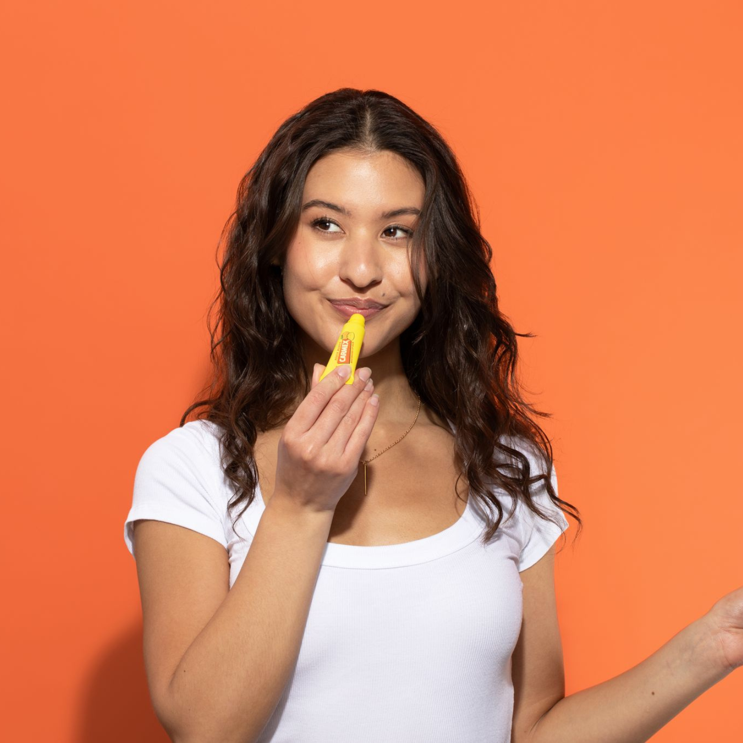 Frau mit Carmex Tube Pfirsich Mango Lippenbalsam vor orangem Hintergrund.