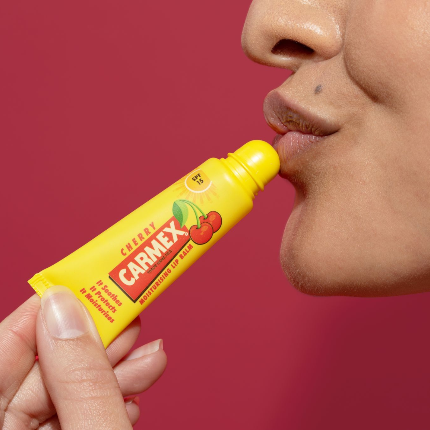 Gelbe Tube CARMEX Cherry Lippenbalsam wird auf Lippen aufgetragen. Lächeln. SPF 15.