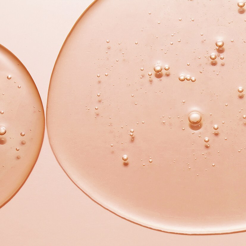 Nahaufnahme: Hyaluronsäure Essenz-Textur. Transparente, roséfarbene Flüssigkeit mit eingeschlossenen Bläschen.