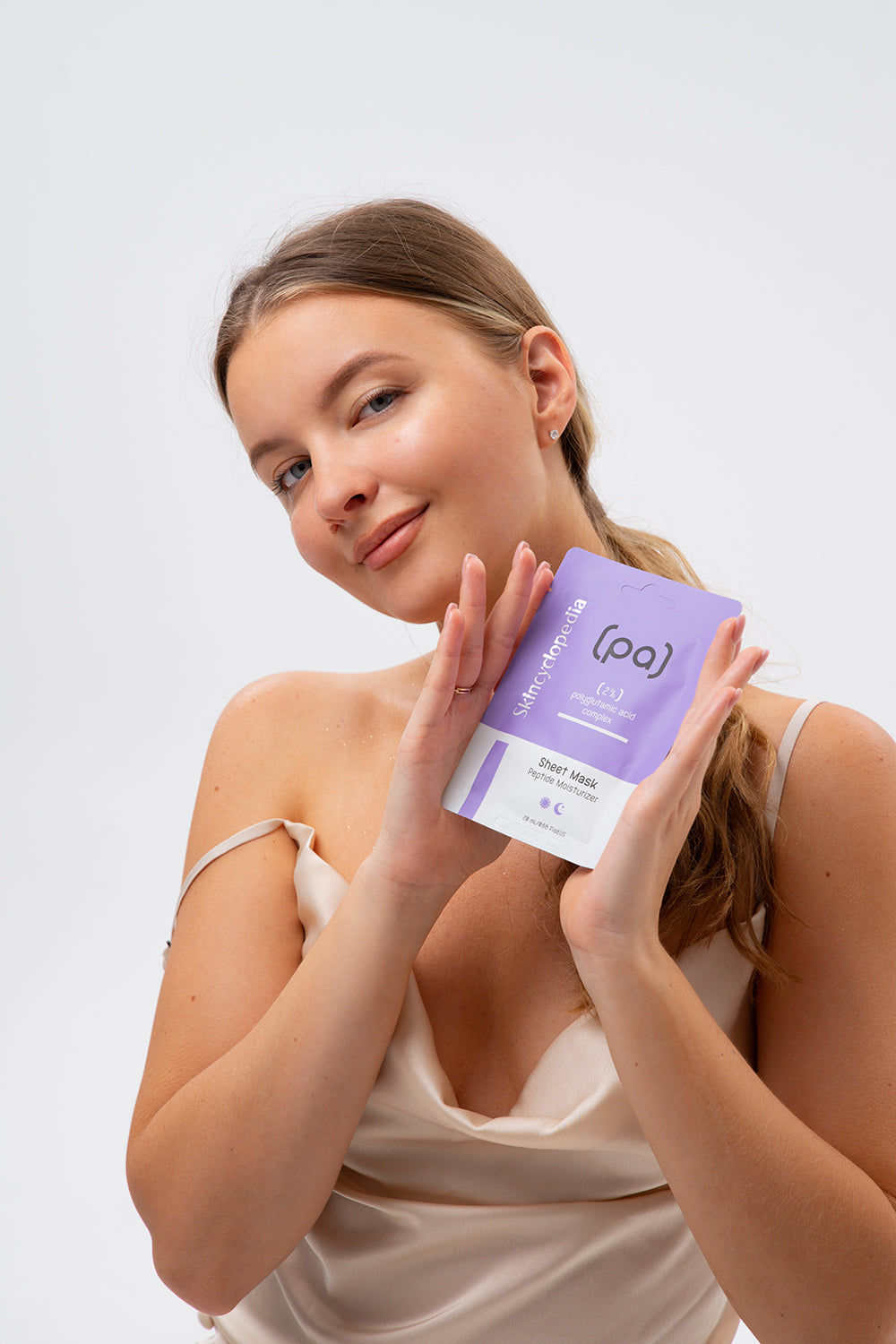 Frau hält SKINCYCLOPEDIA Polyglutaminsäure Sheet Maske in Händen. Die Verpackung ist lila und weiss.