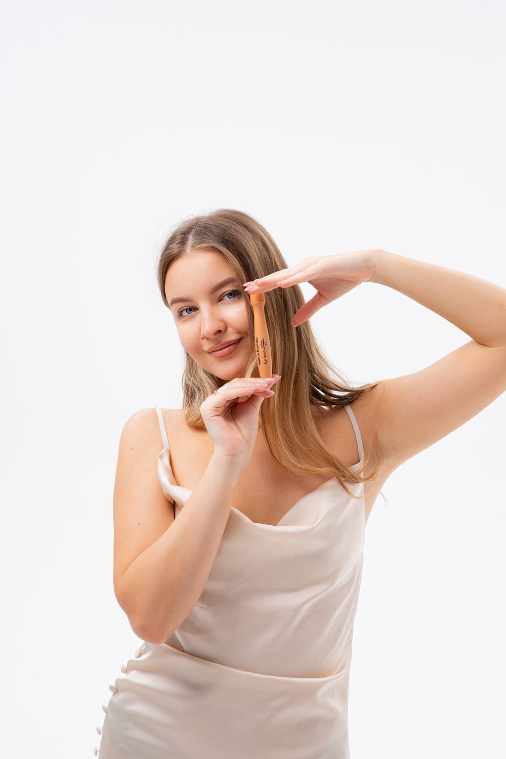 Uma senhora apresenta, com um sorriso, o roll-on para os olhos SKINCYCLOPEDIA com cafeína e Q10, num fundo branco