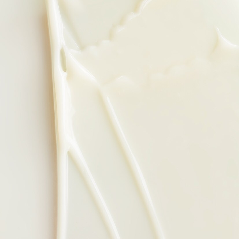 Nahaufnahme einer dicken, cremig-weißen Flüssigkeit mit Schlieren. Die Texturen sind glatt und glänzend.