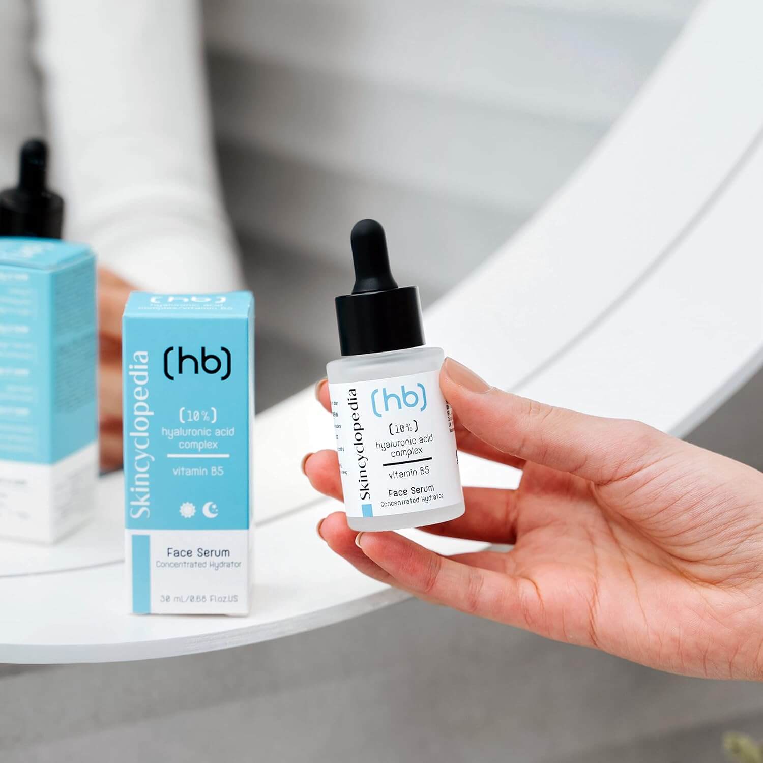 Ein Hand hält SKINCYCLOPEDIA Hyaluron Serum. Daneben die Verpackung. Fokus auf Feuchtigkeit.