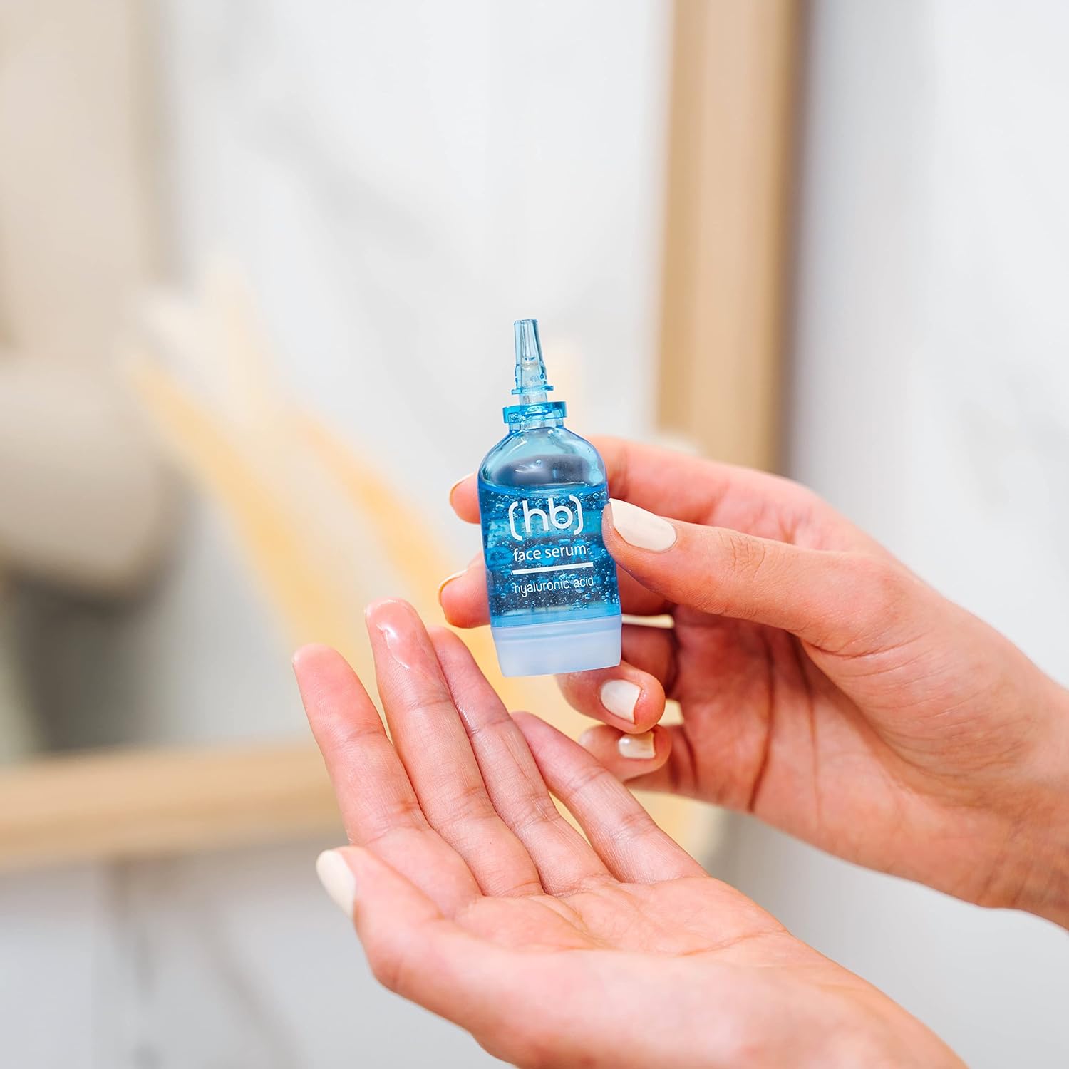 Ein Gesichtsserum mit Hyaluronsäure in blauer Ampulle wird von einer Frau gehalten. Ein Tropfen Serum befindet sich bereits auf ihrer Hand.