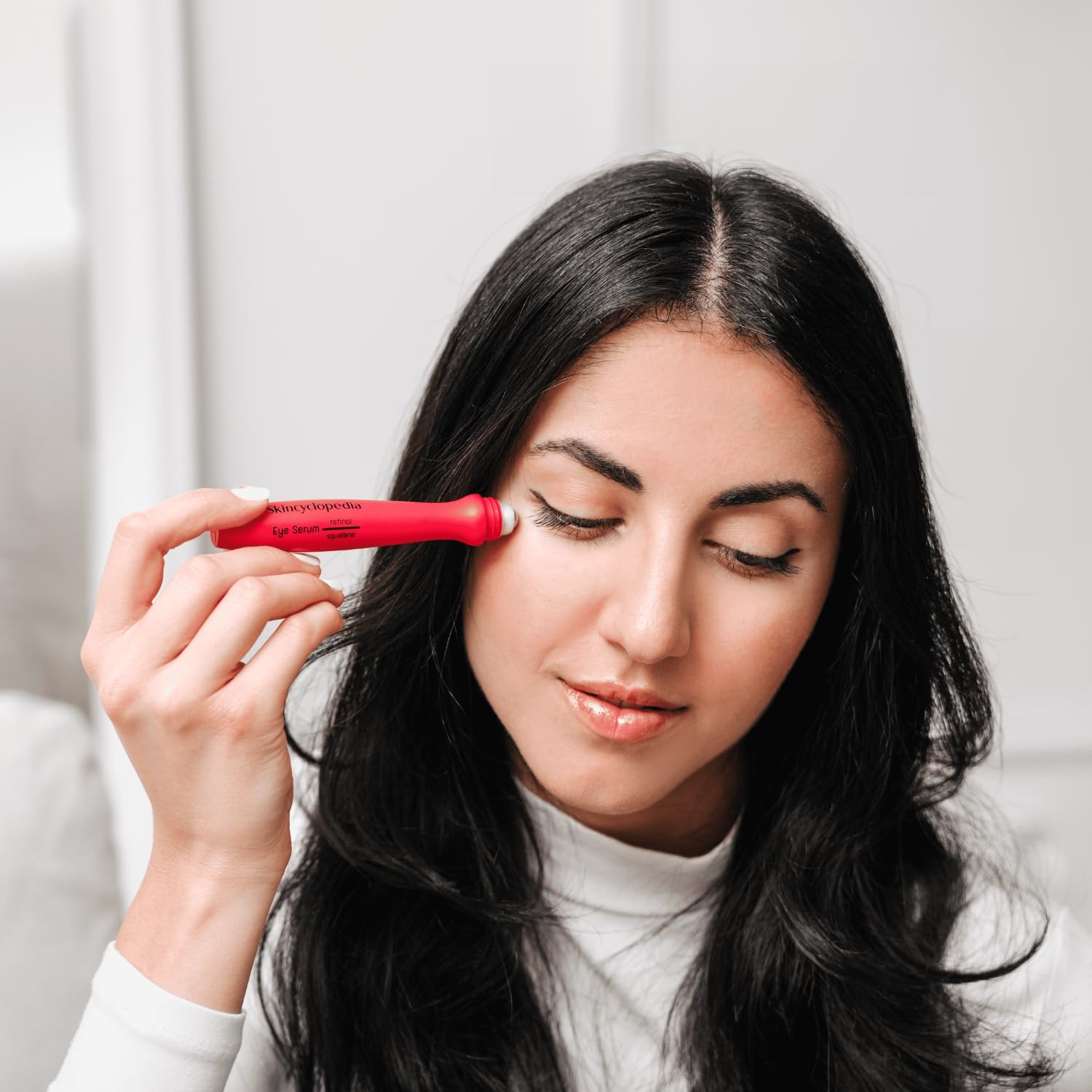 Uma mulher aplica o roll-on de retinol SKINCYCLOPEDIA vermelho na zona dos olhos