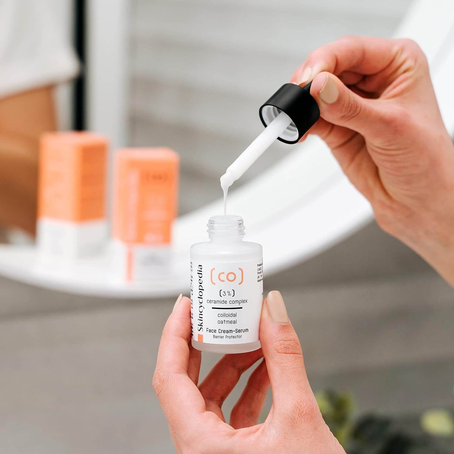 Nahaufnahme: Hände halten SKINCYCLOPEDIA Ceramide Serum Flasche, Serumtropfen aus Pipette.