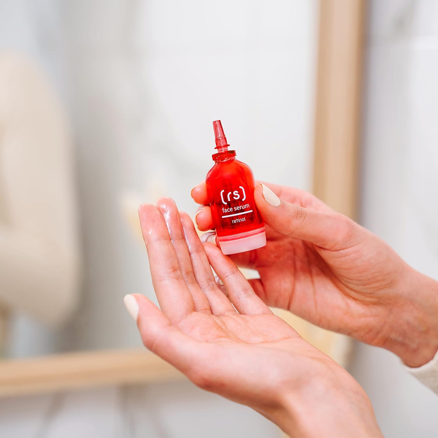 Nahaufnahme: Person hält rotes Retinol Serum von SKINCYCLOPEDIA in der Hand. Text auf der Flasche: "(r.s) face serum, retinol". Serum wird auf die Hand getropft.