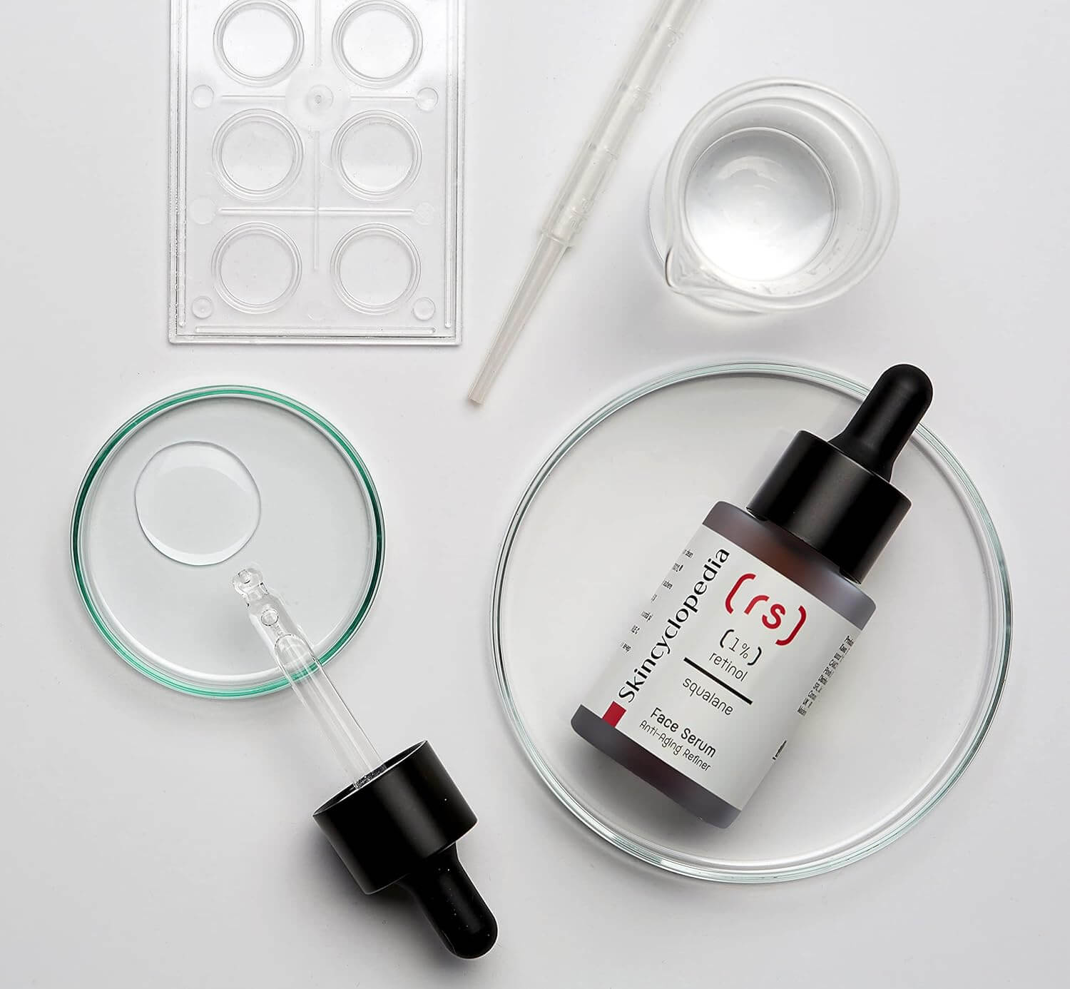 Draufsicht: SKINCYCLOPEDIA Retinol 1% Serum, Pipette, Petrischale mit Tropfen und Laborutensilien. Anti-Aging Nachtserum.