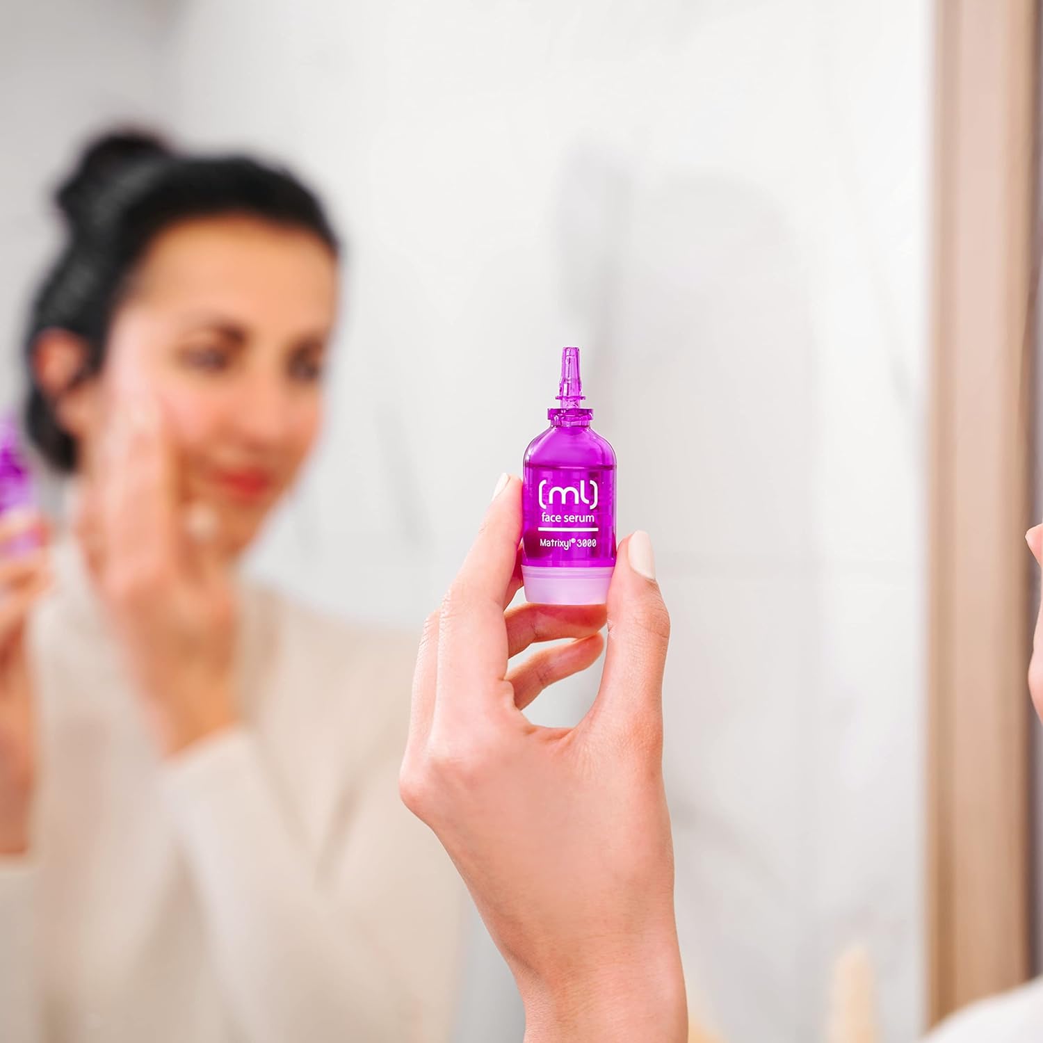 Frau vor Spiegel, hält Matrixyl 3000 Serum. Hautpflege für reife Haut, Teil des SKINCYCLOPEDIA Age Perfect Guide Sets. Anti-Aging Produkt im Fokus.
