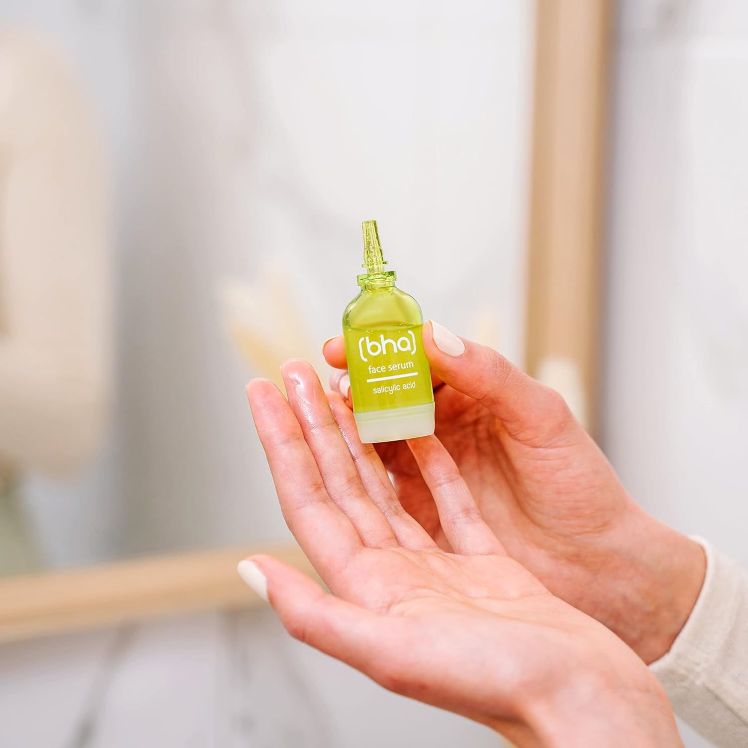 Ein Gesichtsserum in einer kleinen, grünen Glasampulle, gehalten von zwei Händen. Das Etikett ist weiß und trägt den Aufdruck "(bha) face serum".