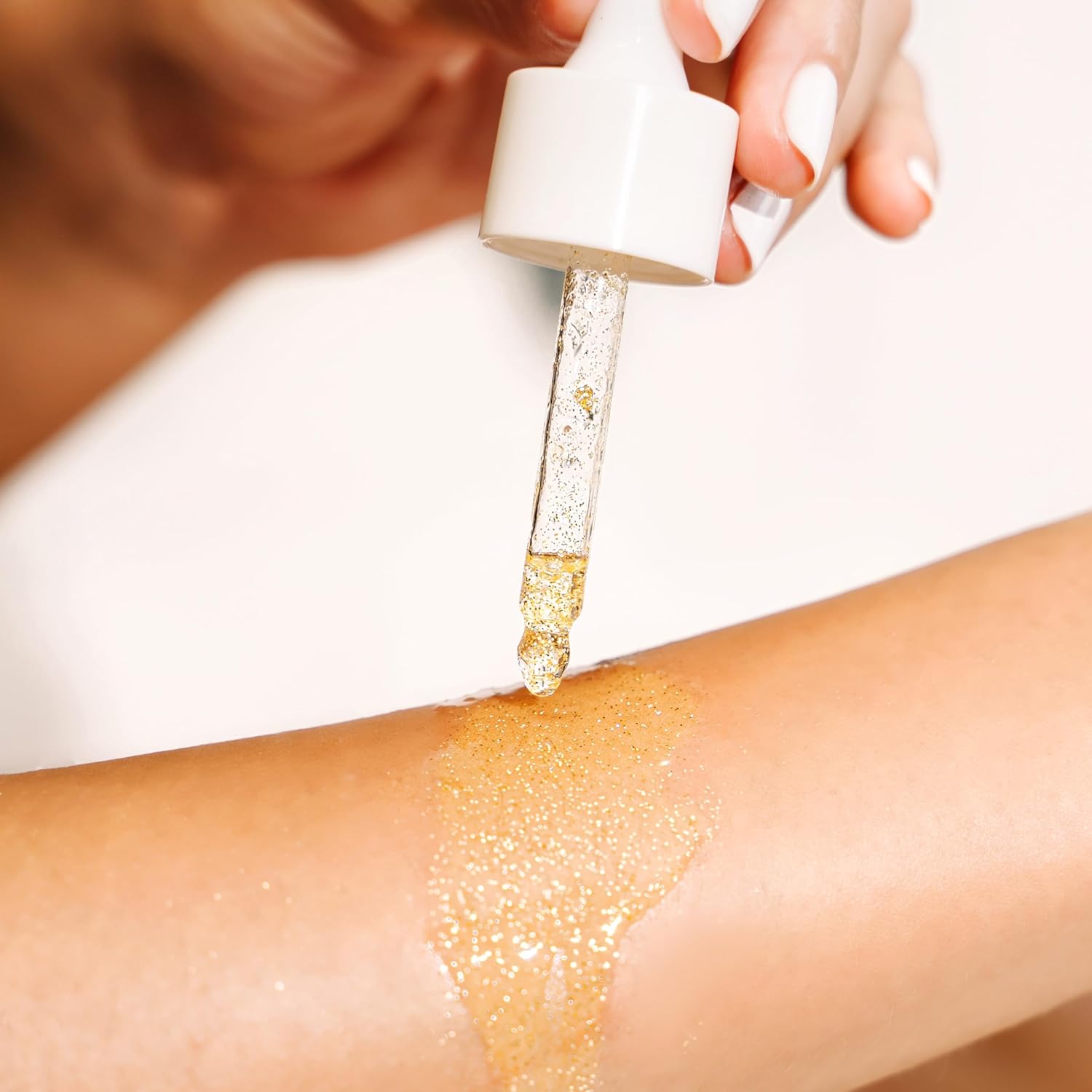 O óleo corporal dourado SKINCYCLOPEDIA Shimmer Body Oil é aplicado diretamente na pele do braço com uma pipeta