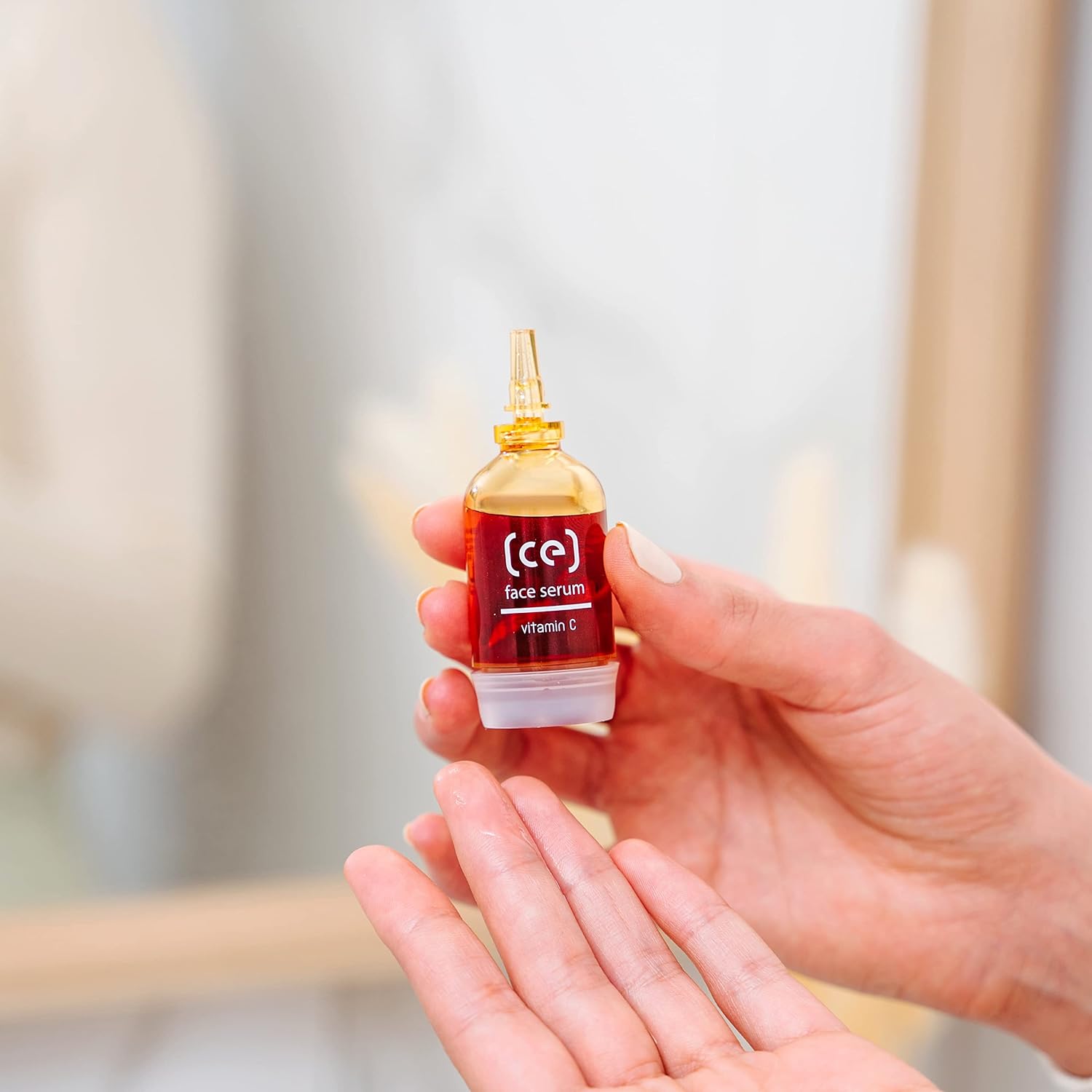 Hautpflege: Hand hält SKINCYCLOPEDIA Serum, rote Flüssigkeit. Text: "face serum, Vitamin C". Handfläche darunter, leichter Glanz.