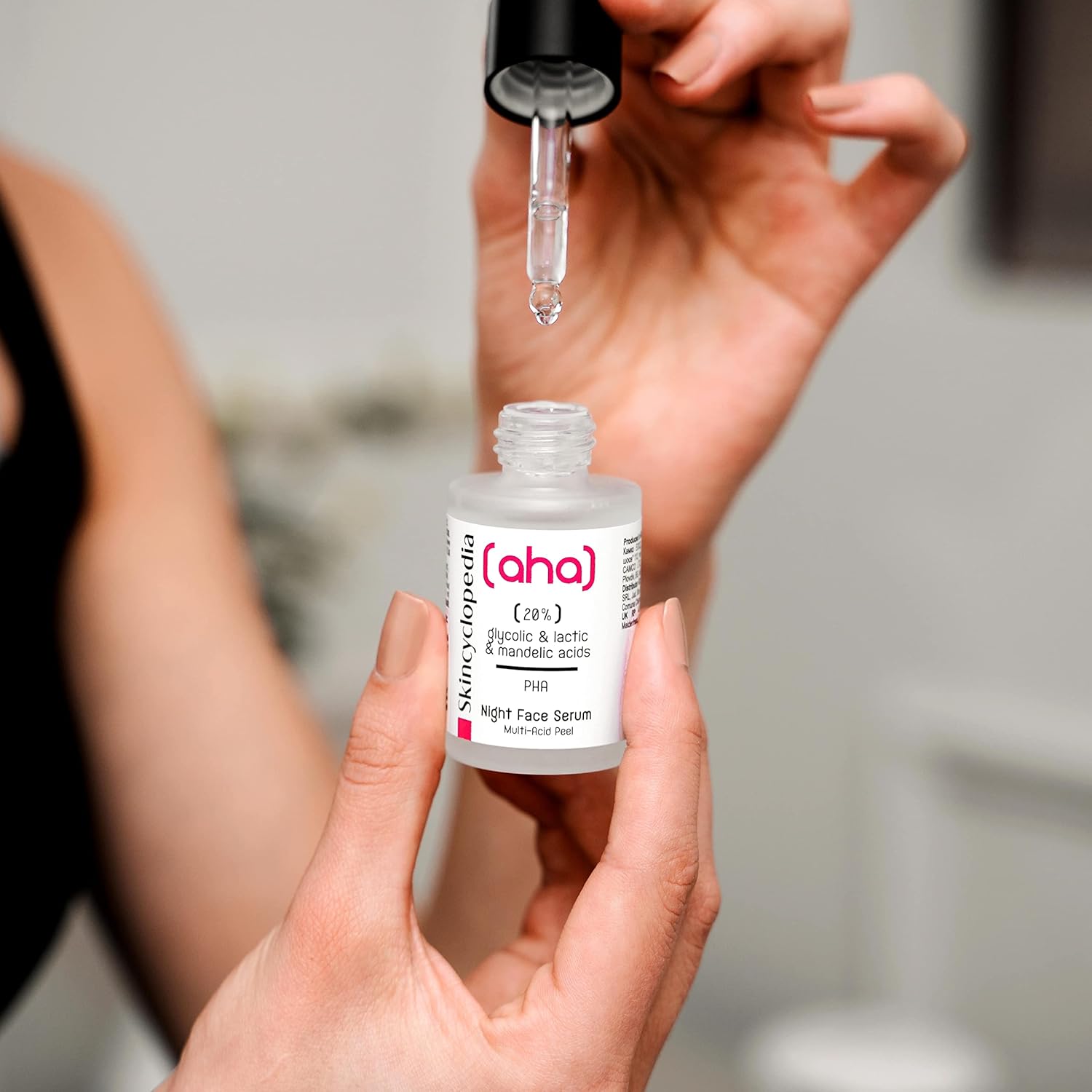 Eine Person hält das SKINCYCLOPEDIA AHA/PHA Peeling Serum. Eine Pipette tropft Serum in die Flasche. Fokus auf Serum und Flasche.