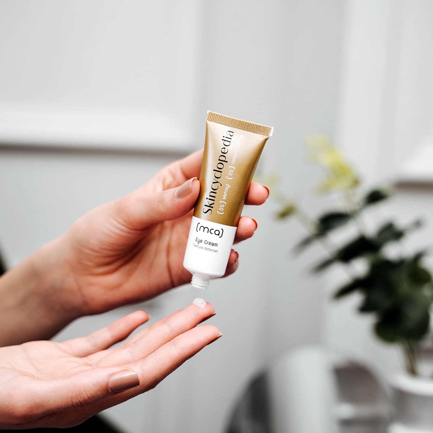 A creme para os olhos SKINCYCLOPEDIA com Matrixyl e cafeína é aplicada com a ponta do dedo a partir de um tubo branco-dourado