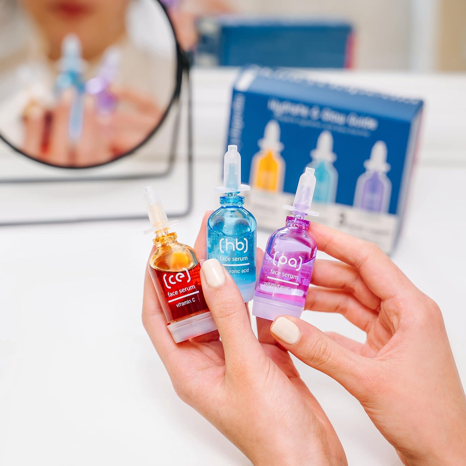Nahaufnahme von drei SKINCYCLOPEDIA Seren in Händen, Teil des Hydrate Guide Sets für intensive Feuchtigkeit. Die Serumflaschen sind orange, blau und lila.