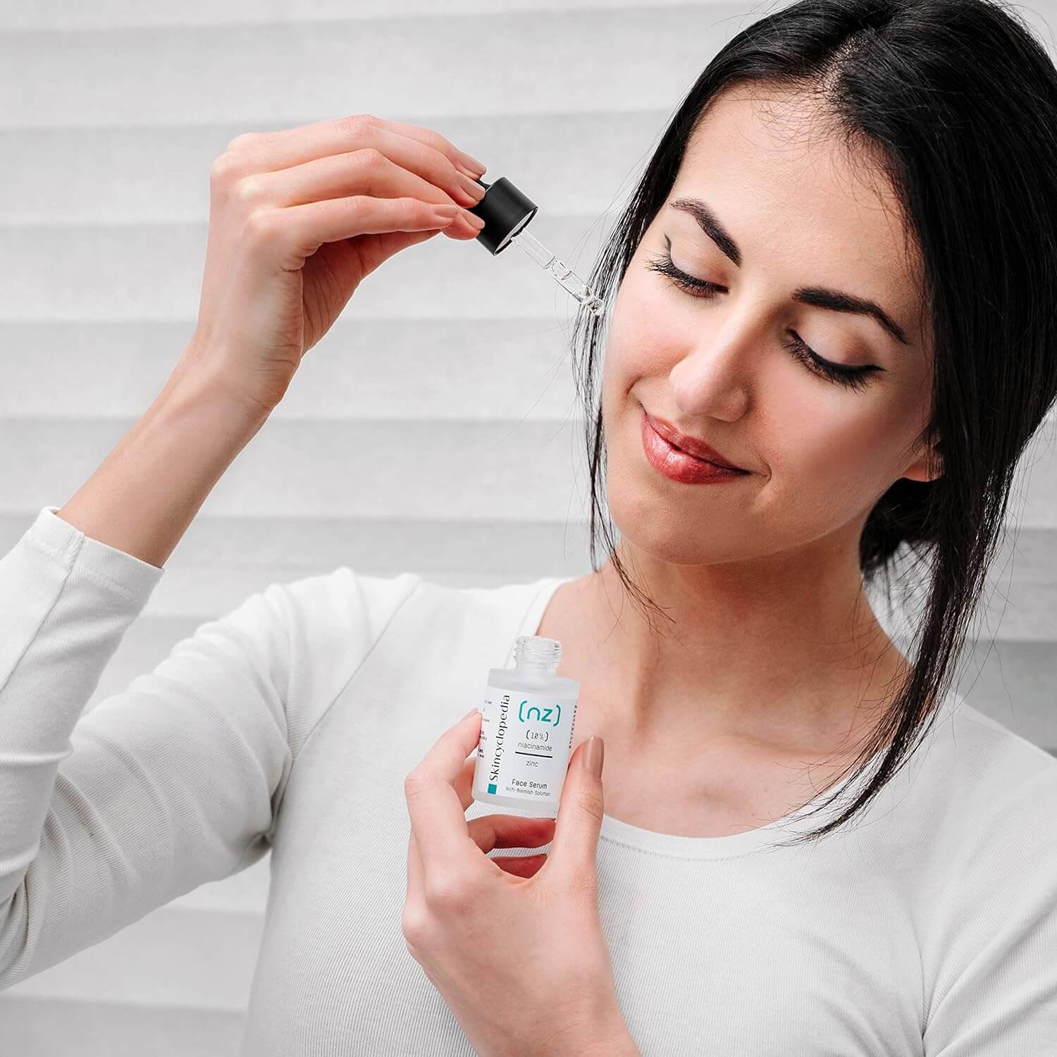 Frau trägt SKINCYCLOPEDIA Niacinamide 10% Serum auf. Sie hält eine Flasche mit Pipette, um Hautbalance zu fördern und Poren zu verfeinern.