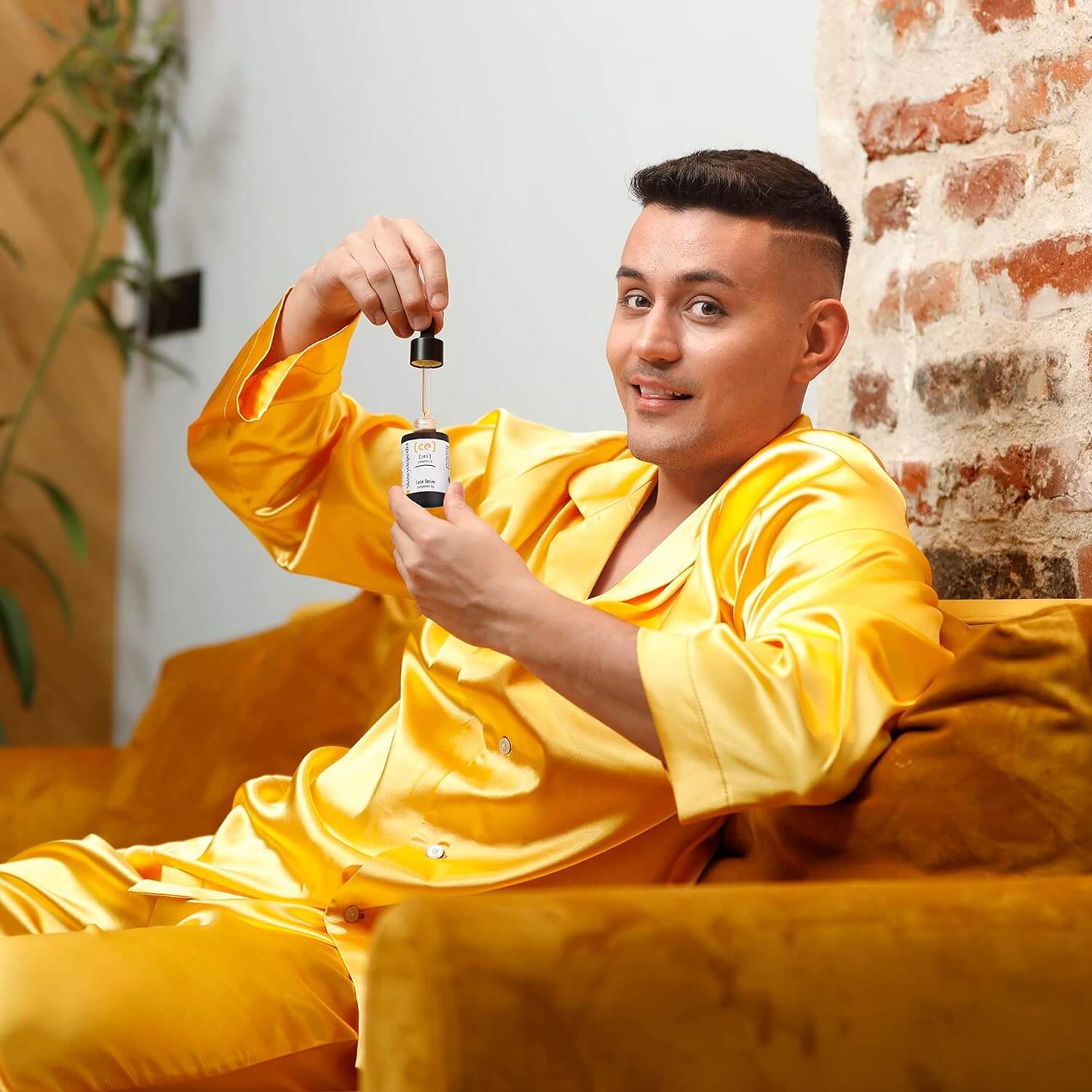 Person im gelben Pyjama hält SKINCYCLOPEDIA Vitamin C Serum. Tropfen hängt an Pipette.