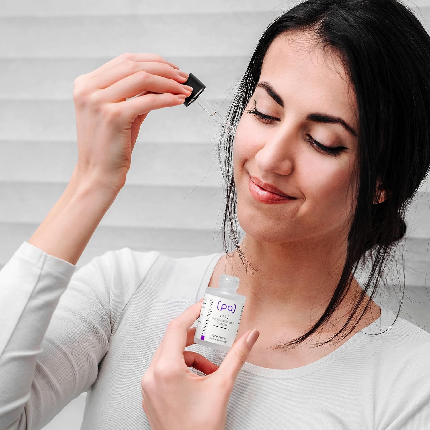 Frau hält SKINCYCLOPEDIA Polyglutaminsäure Serum mit Pipette in der Hand.