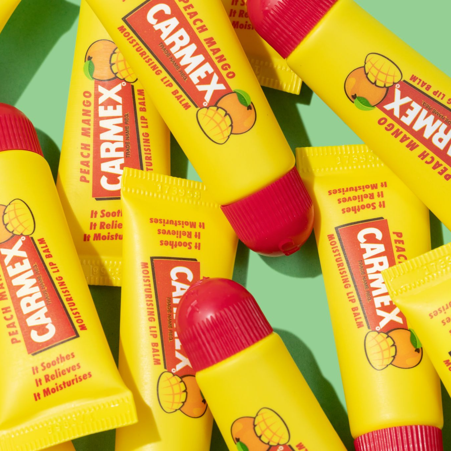 Gelbe Tuben Lippenbalsam von CARMEX Peach Mango, teils überlappend, liegen auf einem hellgrünen Hintergrund. Rote Verschlusskappen sind sichtbar.