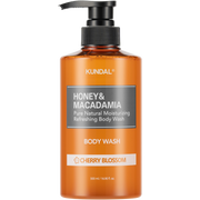 Eine orangefarbene Flasche Körperwaschlotion mit schwarzem Pumpspender. Auf der Flasche steht "Kundal, Honig & Macadamia, Cherry Blossom".