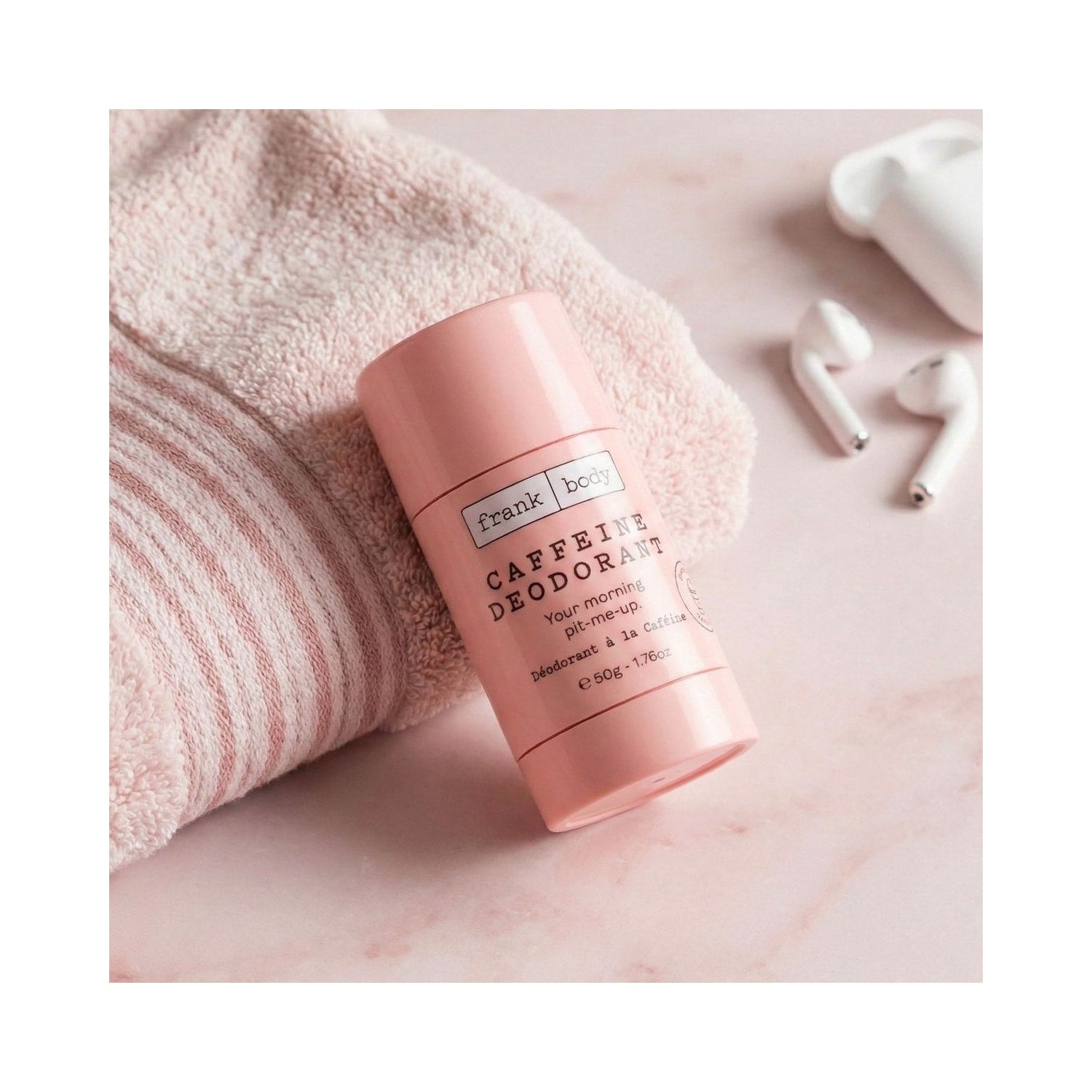 Rosa Stick des FRANK BODY Caffeine Deodorant 50g auf einem hellrosa Handtuch neben weissen kabellosen Kopfhoerern