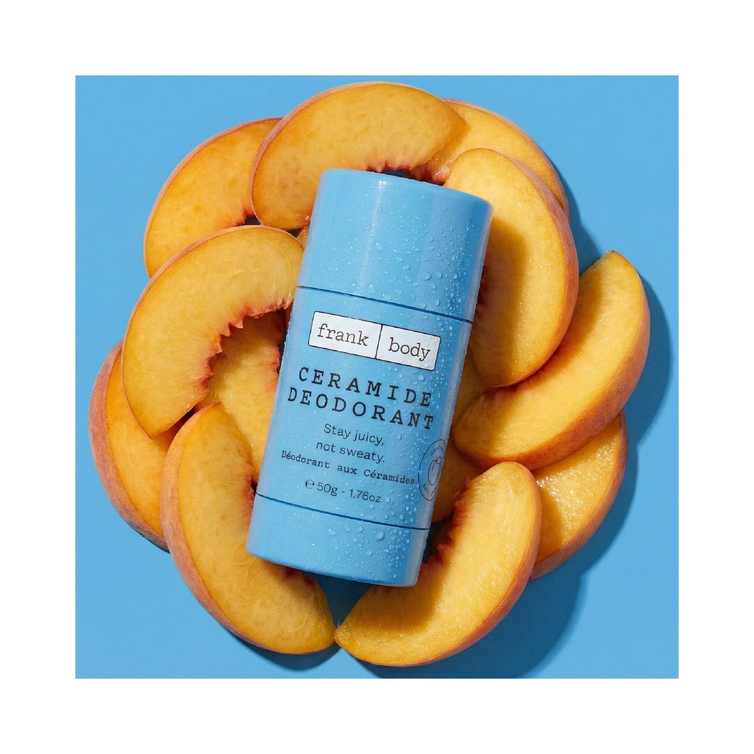 Hellblauer FRANK BODY Ceramide Deodorant Stick mit Wassertropfen, umgeben von frischen Pfirsichspalten auf blauem Grund