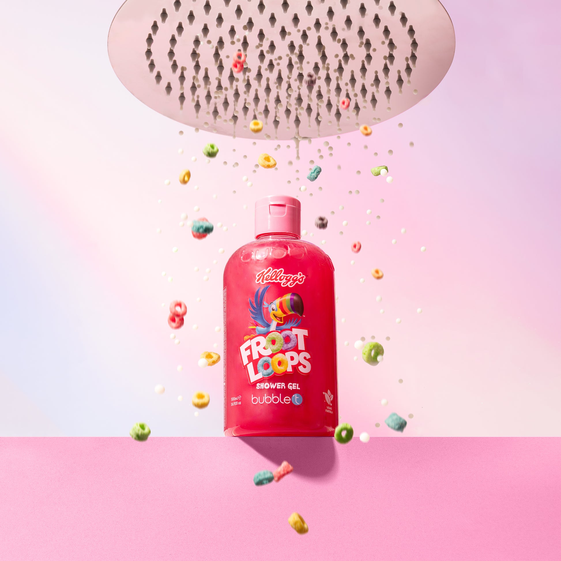 Ein Duschkopf über einer Flasche BUBBLE T Froot Loops Duschgel, umgeben von bunten Fruchtringen und Seifenblasen vor rosa Hintergrund.