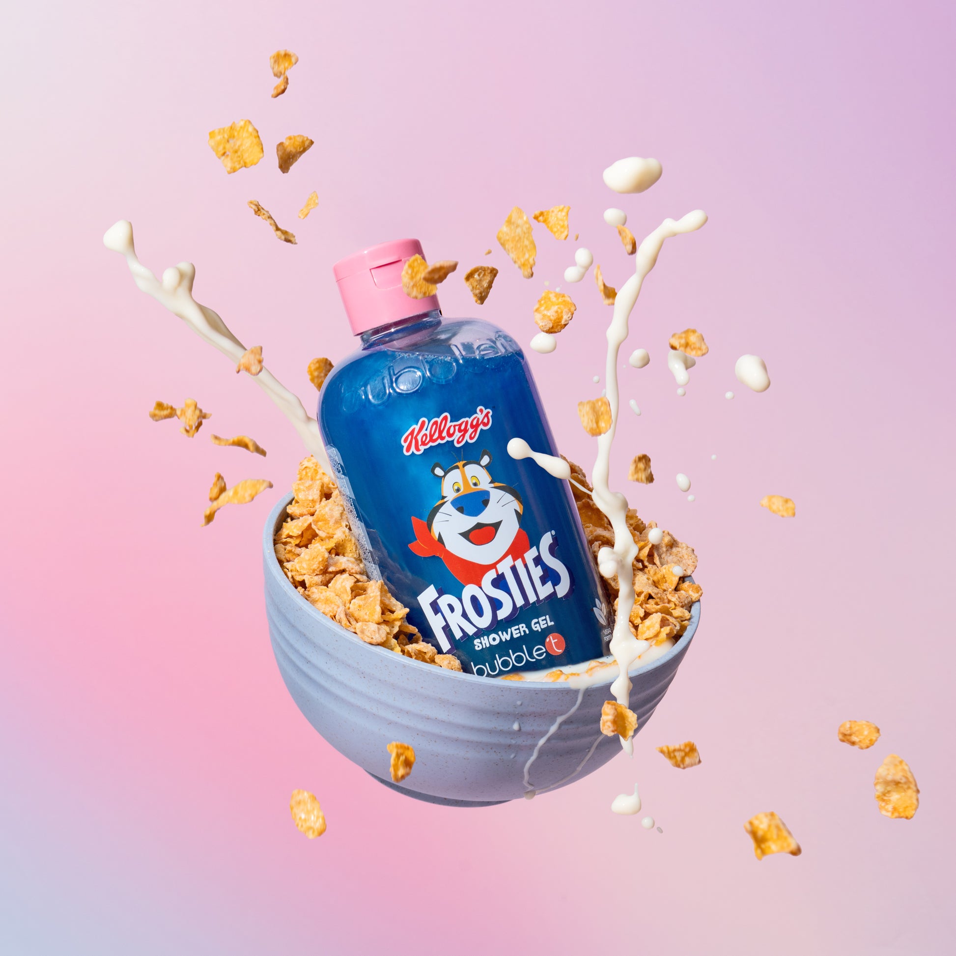 Ein blauer BUBBLE T Frosties Duschgel Flasche in einer Schale voller Cornflakes mit Milchspritzern vor rosa-lila Hintergrund.