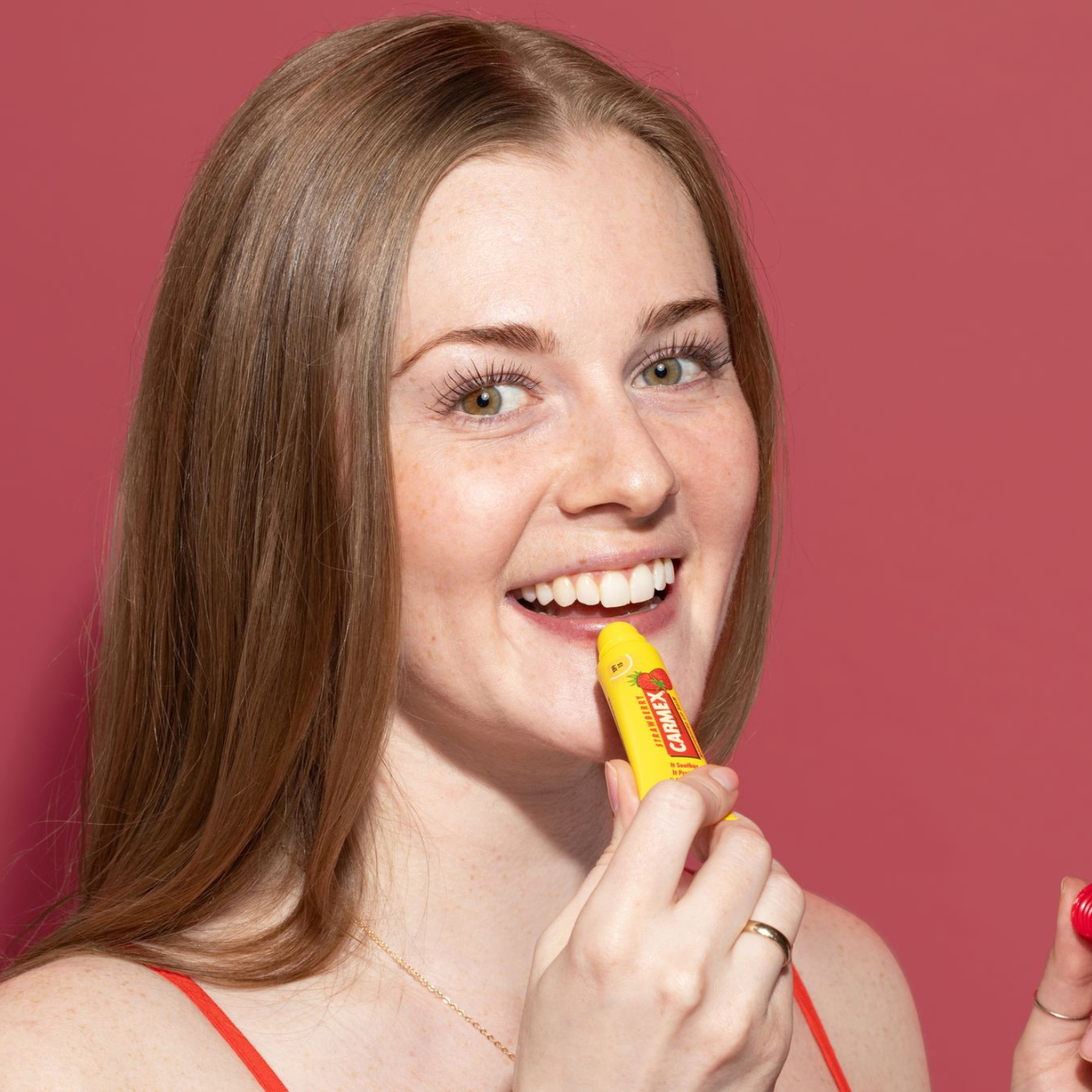 Frau trägt CARMEX Strawberry Lippenbalsam Tube auf. Gelbe Tube mit Erdbeer-Motiv.