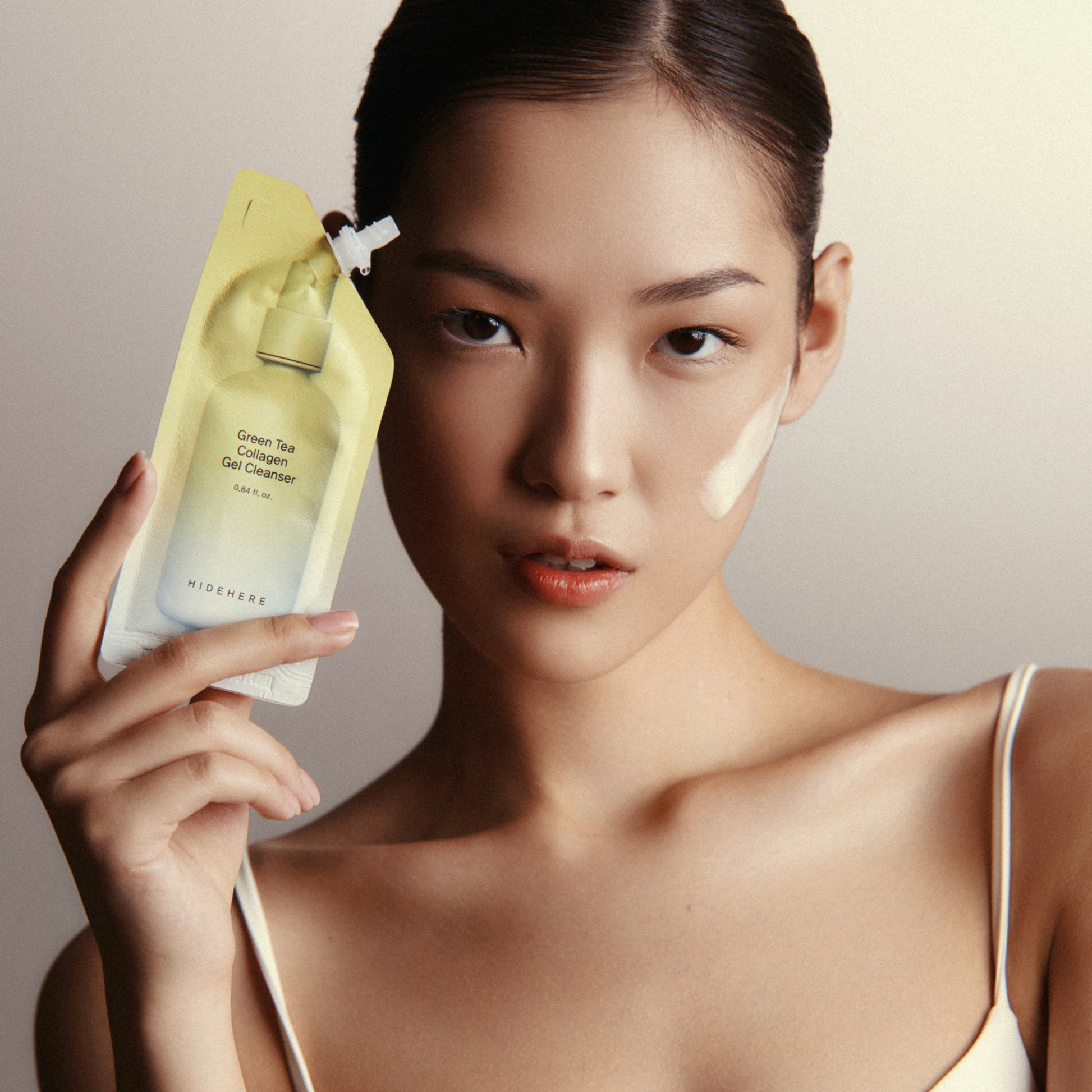 Asiatische Frau hält HIDEHERE Green Tea Collagen Gel Cleanser. Gel-Textur auf der Wange.