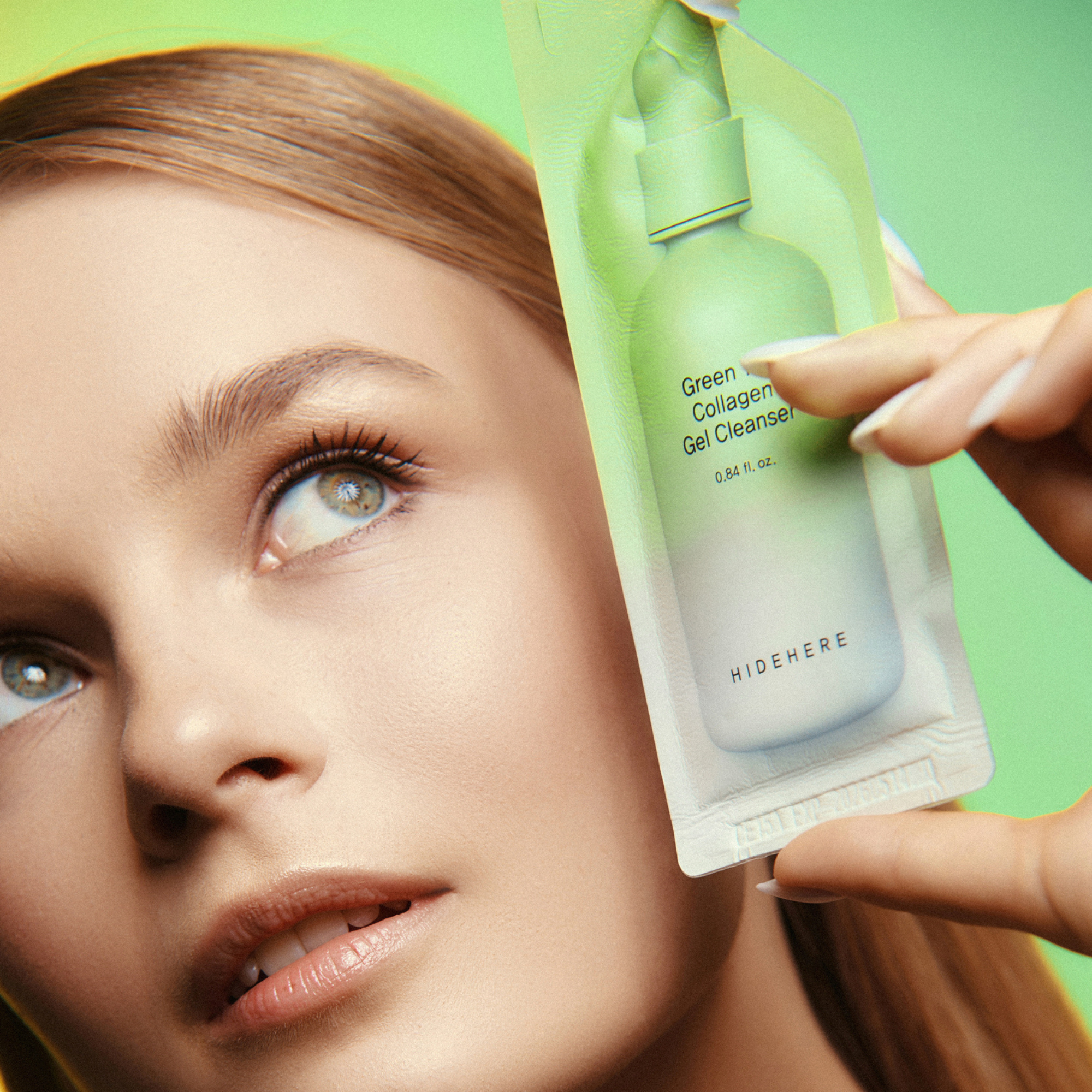 Porträt einer jungen Frau, die ein HIDEHERE Green Tea Collagen Gel Cleanser Produktmuster in den Händen hält. Der Hintergrund ist hellgrün.