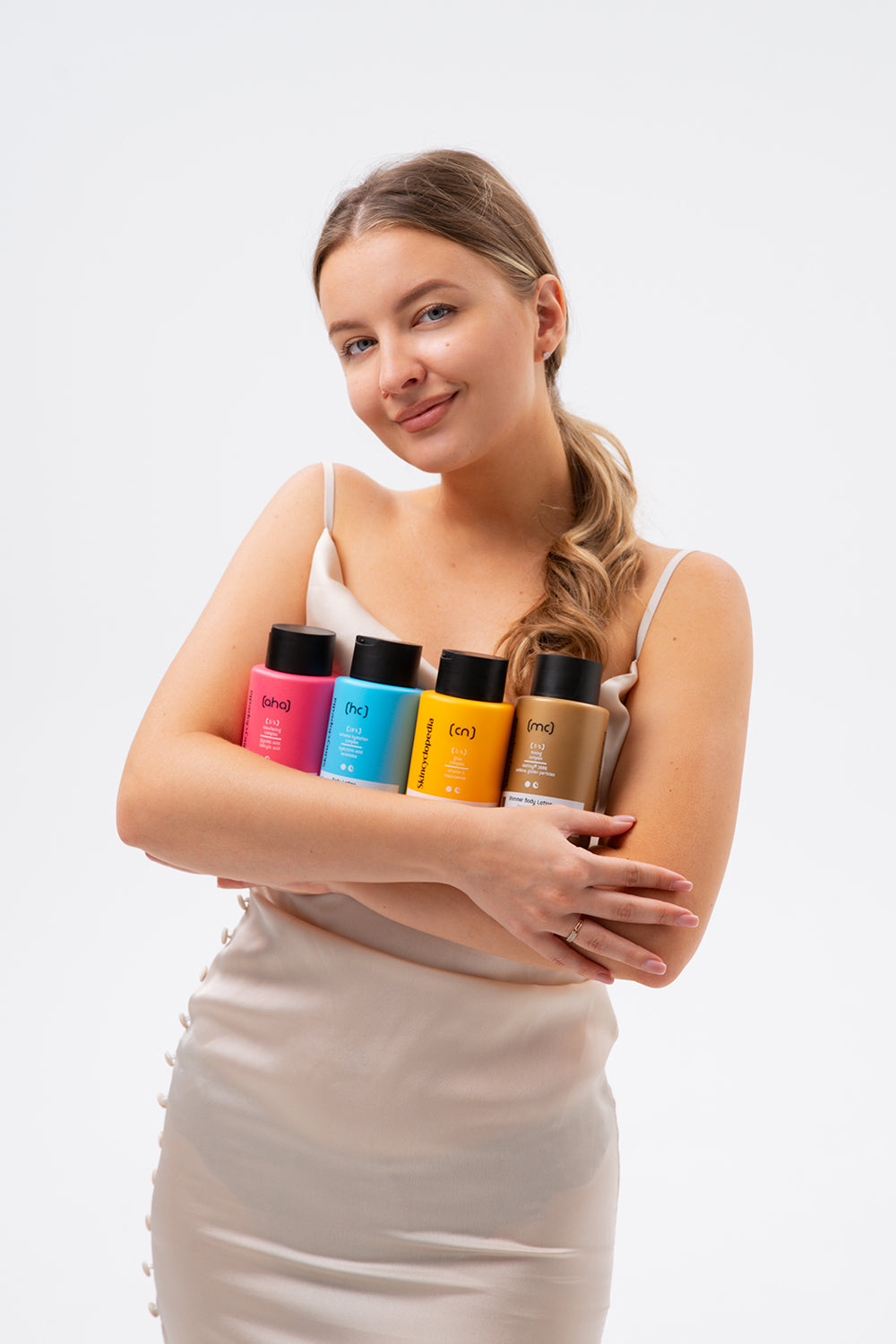 Frau hält SKINCYCLOPEDIA Glow Body Lotions in Rosa, Blau, Gelb und Beige. Fokus auf Glow-Komplex für strahlende Haut.