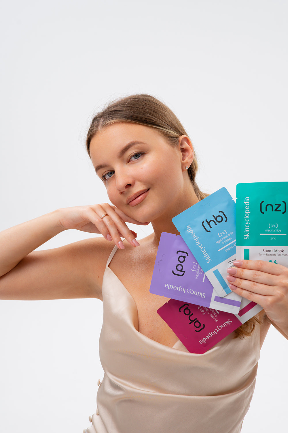 Frau mit SKINCYCLOPEDIA AHA/PHA Sheet Masken in der Hand. Die Packungen sind pink, lila, blau und grün. AHA/PHA steht gut lesbar auf den Packungen.