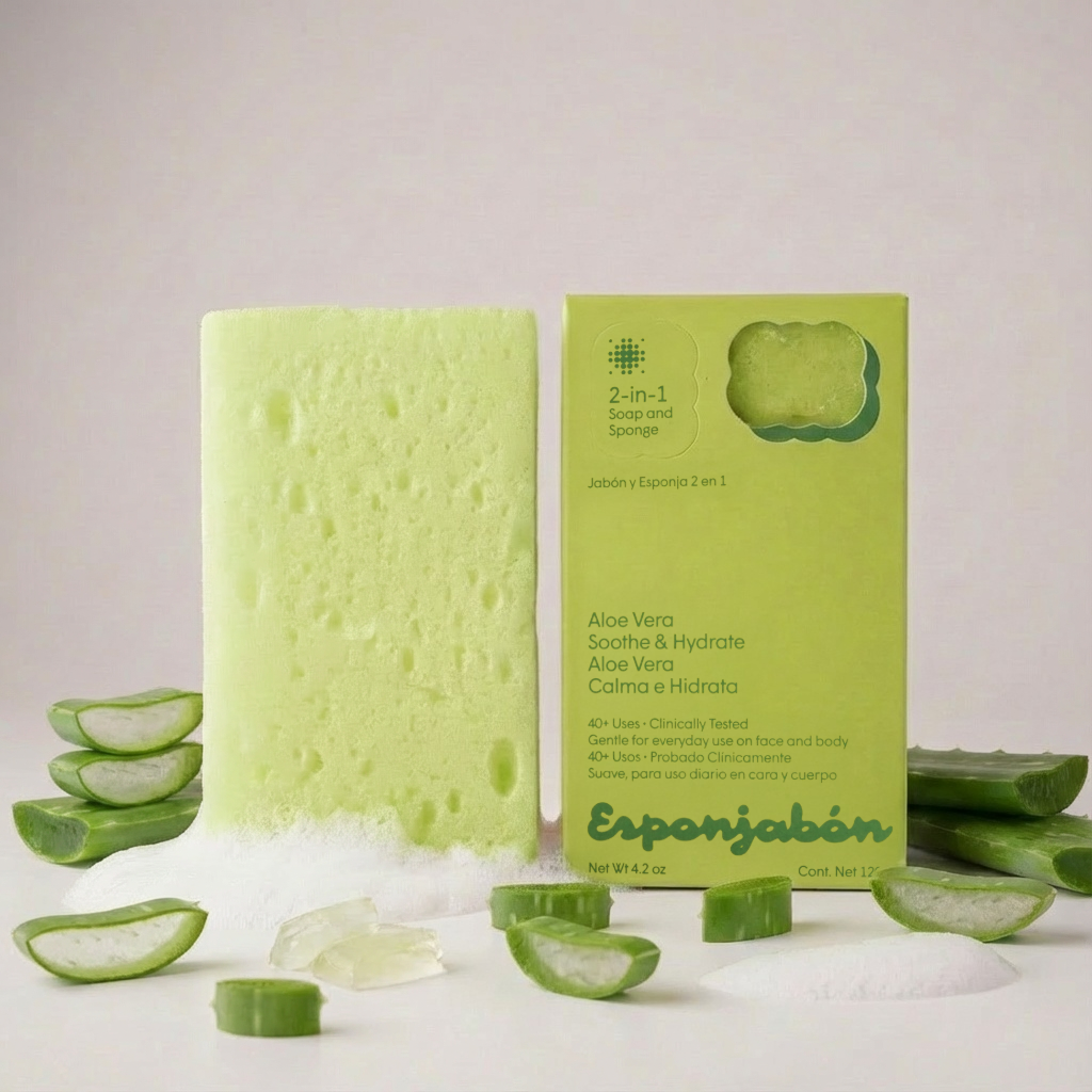 Hellgrüner Badeschwamm mit Seife, neben Produktverpackung und Aloe Vera-Stücken. Schaum und Aloe-Gel liegen verstreut auf hellem Grund.