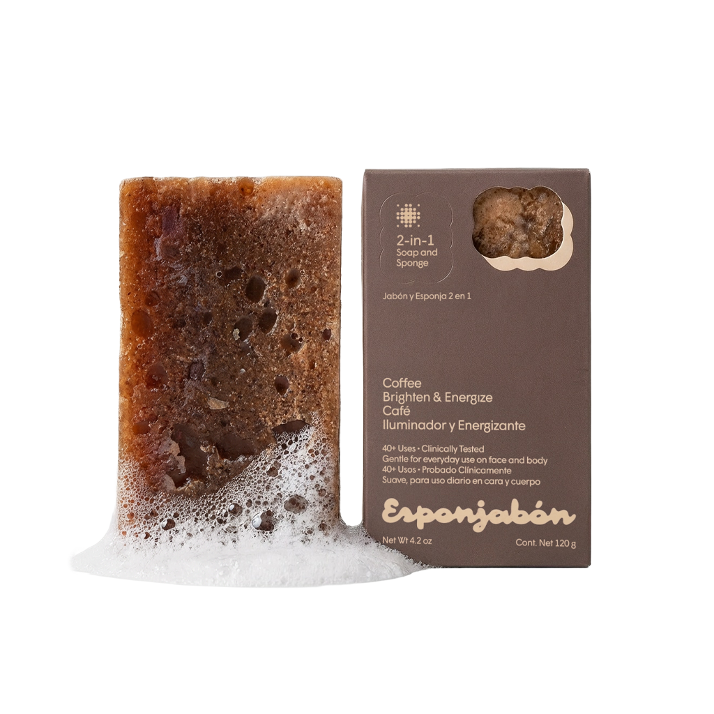 Ein rechteckiges Kaffeeseifenstück mit Schaum daneben eine braune Seifenverpackung mit Sichtfenster und Produktinformationen.