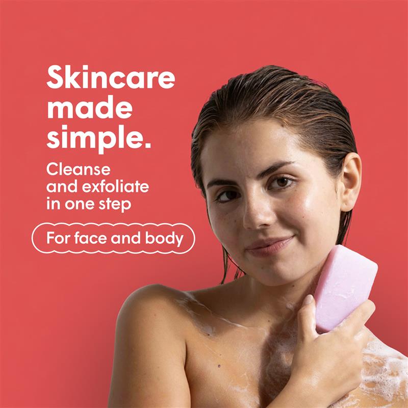 Junge Frau mit seifigem Arm und Schulter, die ein rosafarbenes Seifenstück an ihren Hals hält. Roter Hintergrund mit dem Text "Skincare made simple. Cleanse and exfoliate in one step. For face and body."