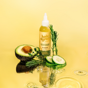 HAIR SYRUP Growsmary Pre-Wash Haaröl umgeben von Rosmarin, Avocado und Gurkenscheiben auf spiegelndem, gelbem Wasser