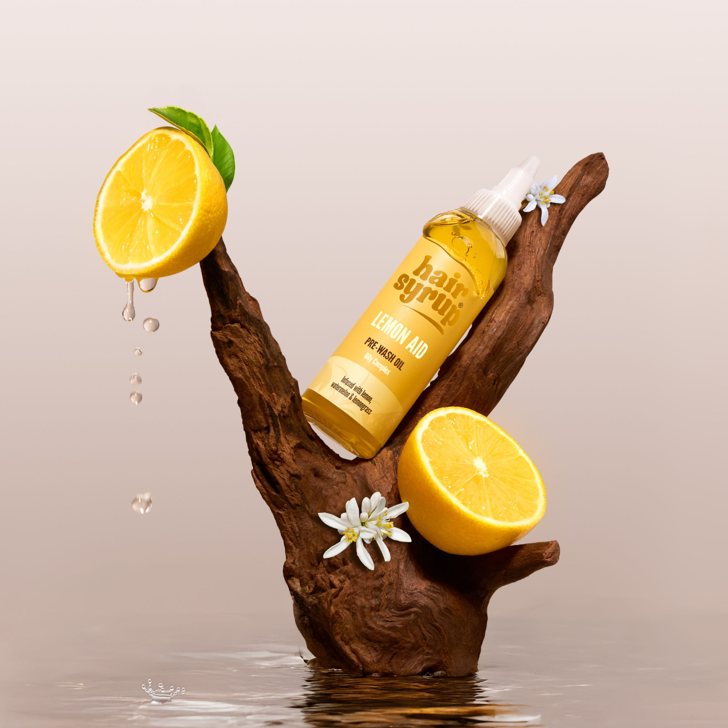 Haarpflegeöl "Lemon Aid" auf einem Holzstück mit Zitronenscheiben und Blüten, mit Spritzwasser, vor beigem Hintergrund.