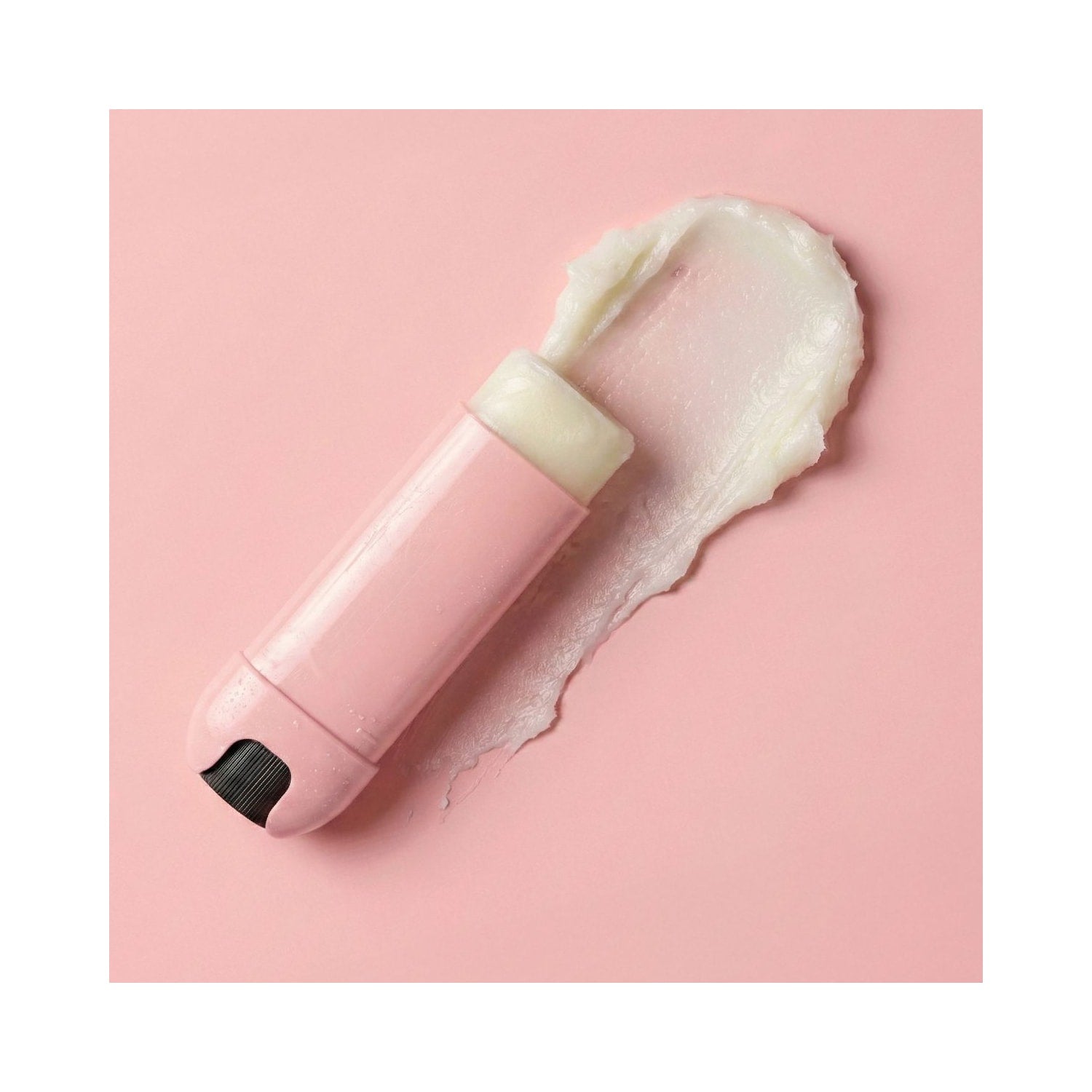 FRANK BODY Original Lip Treatment Lippenpflege-Stift in Rosa mit einer cremigen Textur-Probe auf rosa Hintergrund