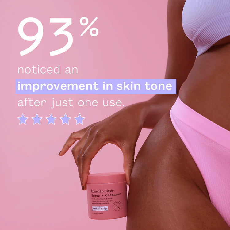 Eine Hand hält den rosa Tiegel des FRANK BODY Rosehip Body Scrub + Cleanser an der Hüfte einer Frau vor pinkem Hintergrund