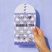 Hand hält lila Bubble T Jasmine Sheet Maske. Aufdruck: Punkte, "Jasmine Bubble Tea Sheet Mask", Bubble Tea Becher, Warnhinweis.