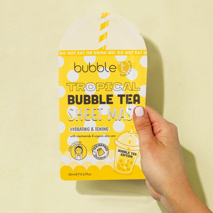 Gelbe Tuchmaske "Tropical Bubble Tea" in Hand gehalten. Verpackung in Form eines Bubble Tea, mit Aufschrift und grafischen Elementen.
