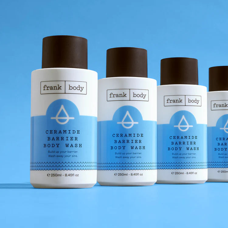 Vier weiße Flaschen FRANK BODY Ceramide Barrier Body Wash mit braunem Deckel vor blauem Hintergrund
