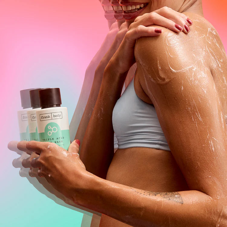 Eine Frau beim Einseifen mit der Flasche FRANK BODY Triple Acid Body Wash vor einem farbenfrohen Hintergrund