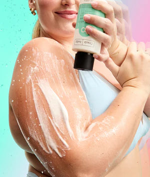 Eine Frau trägt das schäumende FRANK BODY Triple Acid Body Wash auf ihren Arm auf und hält die Flasche