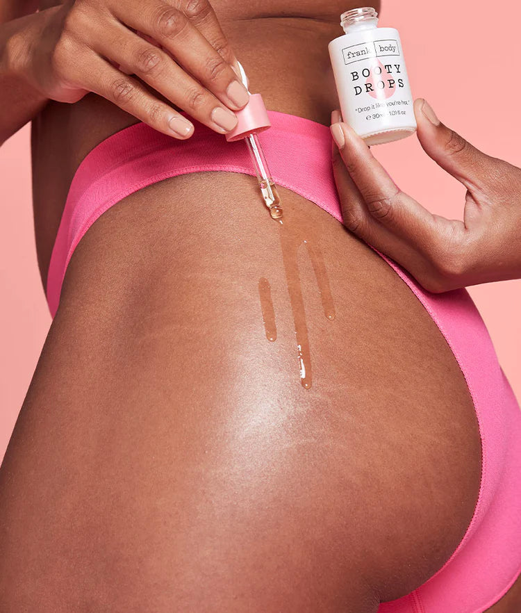 Anwendung der FRANK BODY Firming Booty Drops mit einer Pipette auf dem Gesäß einer Frau in pinkem Slip