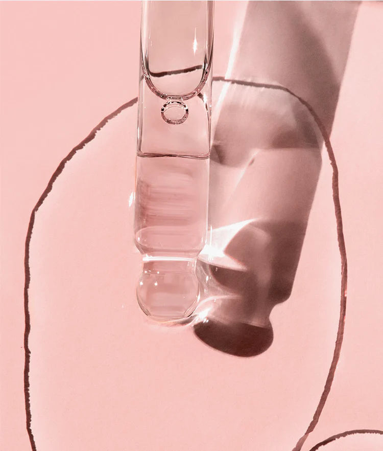 Eine Glaspipette über einer Pfütze aus klarem Serum auf rosa Hintergrund für FRANK BODY Firming Booty Drops