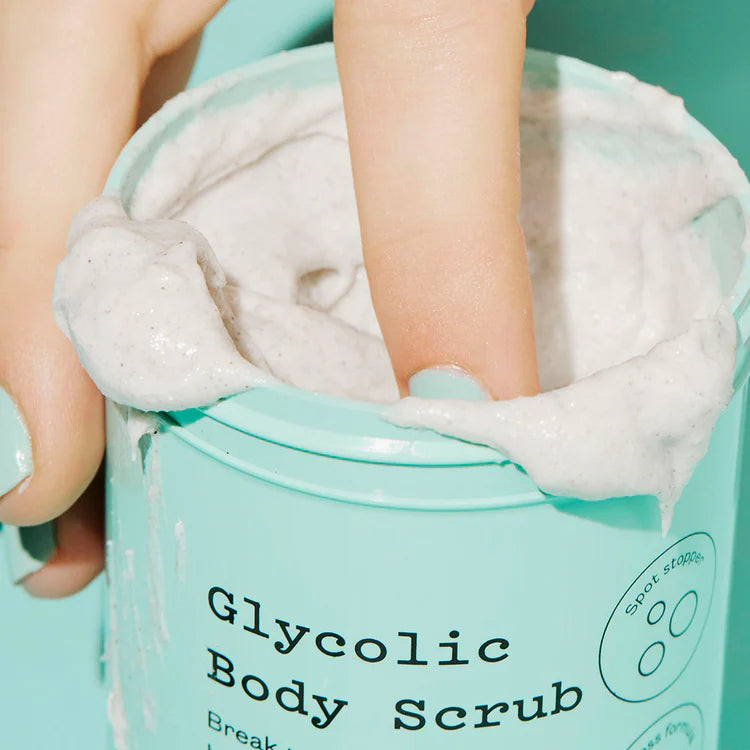 Ein Finger taucht in die cremige, weiße Peeling-Masse im mintgrünen Tiegel des FRANK BODY Glycolic Body Scrub